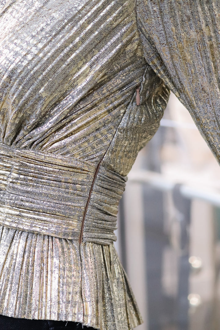 A closeup of a the side zipper of a metallic gold pleated top.